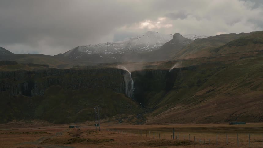 Water falls off dark mountains as gray clouds pass overhead partly flowing upwards