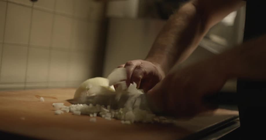 A man is in a kitchen and cutting onions