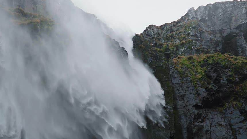 A waterfall flowing over a rocky cliffside and creating mist