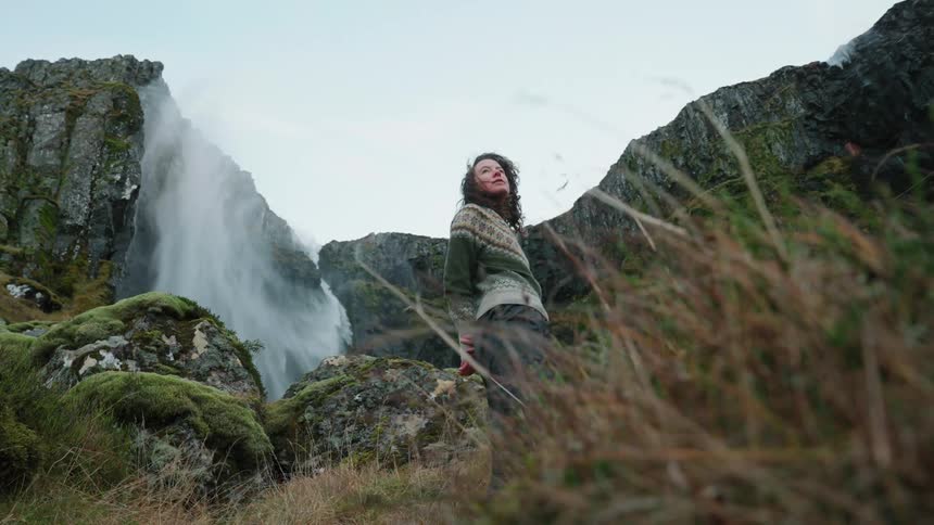 A woman is standing outdoors near mountains
