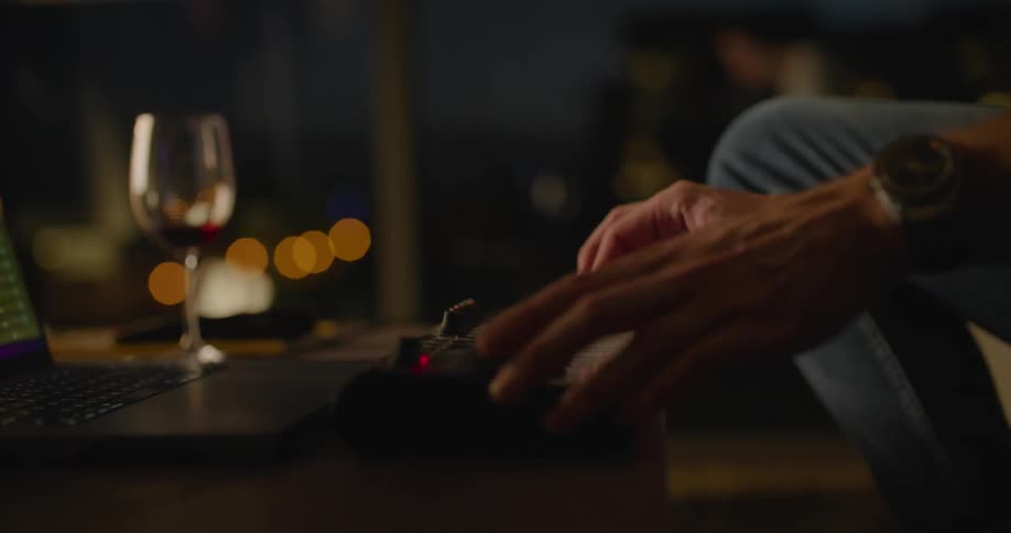 Close up of a musician playing a musical keyboard in front of a laptop in the living room at night
