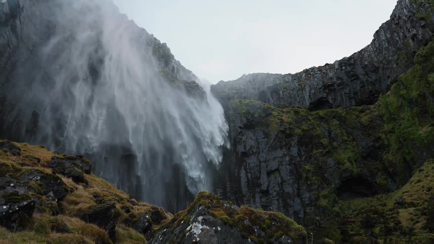 Wind blowing the stream of a waterfall on the cliffs at evening