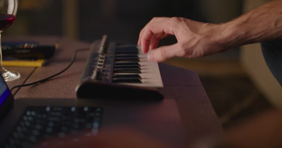 A man is sitting at a table typing on a laptop computer and playing a small electronic keyboard