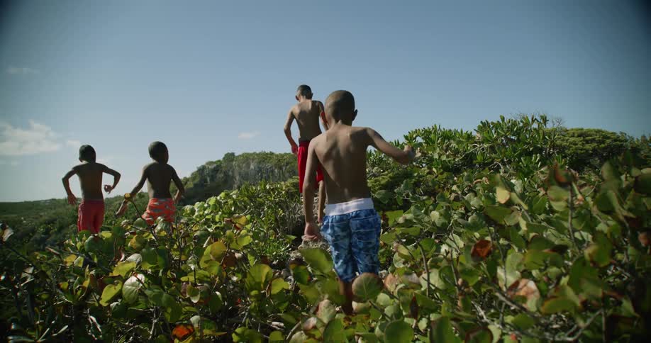 Group of boys wearing swimsuits climb a small hill near the beach