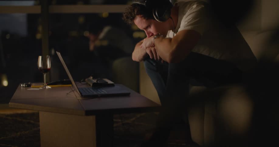 A young white man is sitting down on his couch and on his laptop
