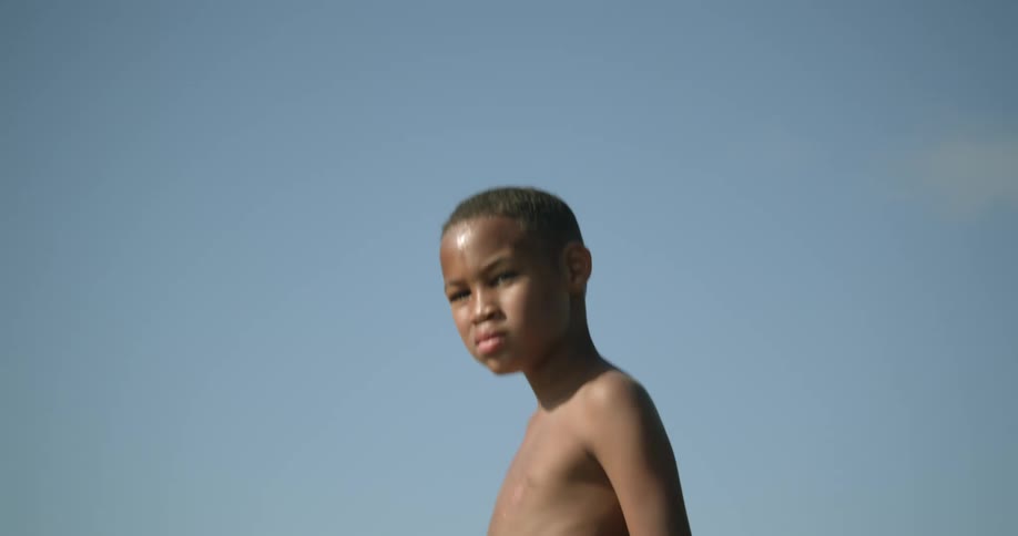 Boy wearing shorts stands on cliff under a blue sky
