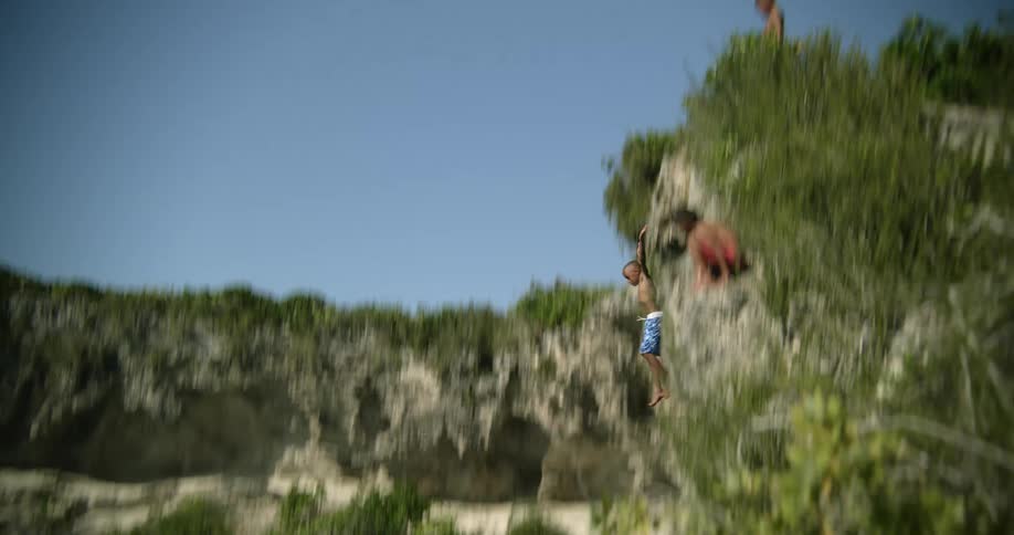 A boy jumps off a cliff and into the water below