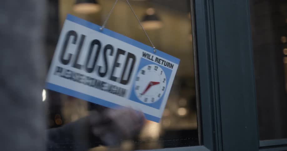 Store owner turns the open sign on the door to closed