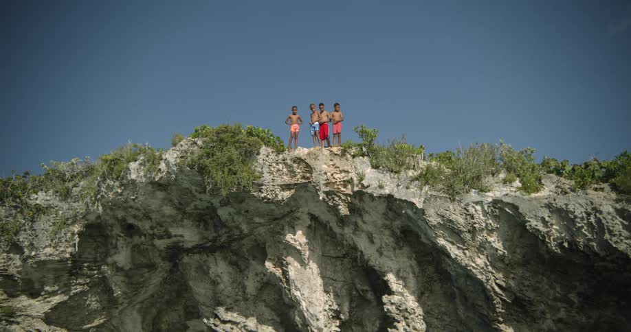Four young boys standing on a cliffside edge in swim trunks