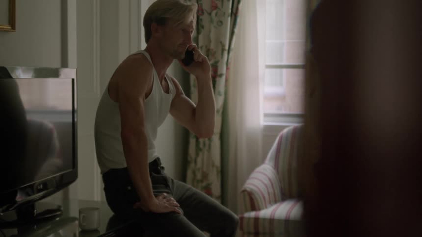A young white man is sitting down and is talking on the phone