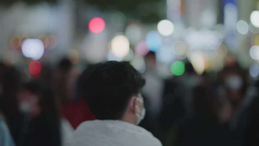 Unrecognizable anonymous people wearing masks walk down the street in downtown area