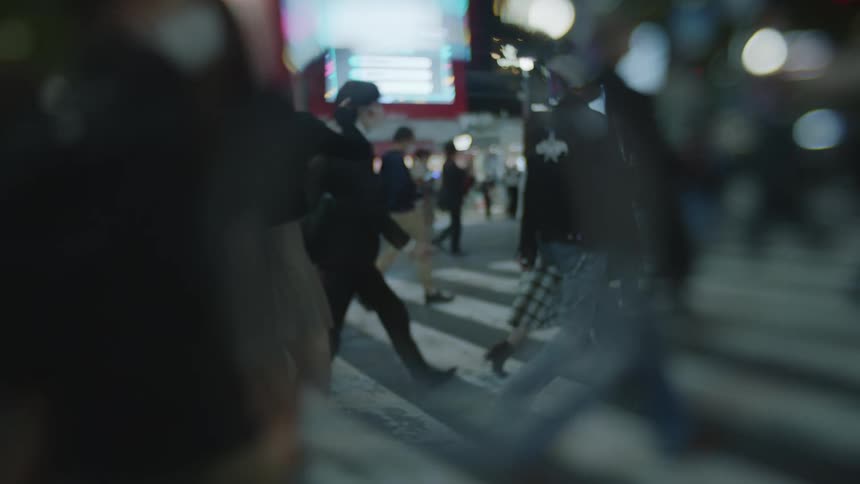 Crowds of people cross a large intersection in a city at night