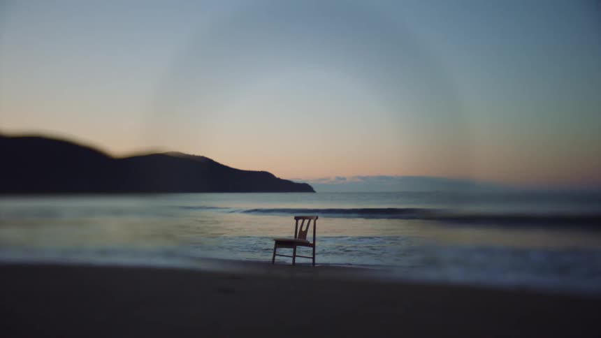 Waves crash into a wooden chair sitting on the beach