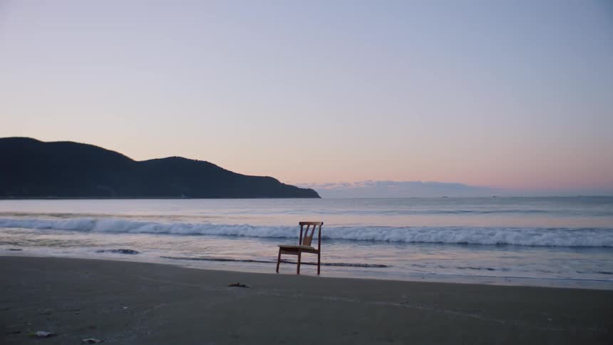 A chair sits on an empty beach as waves roll in to the shore