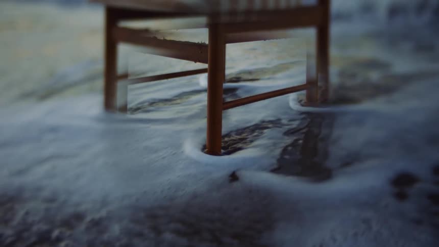 Ocean waves wash around the legs of a wooden chair on a sandy beach during the day