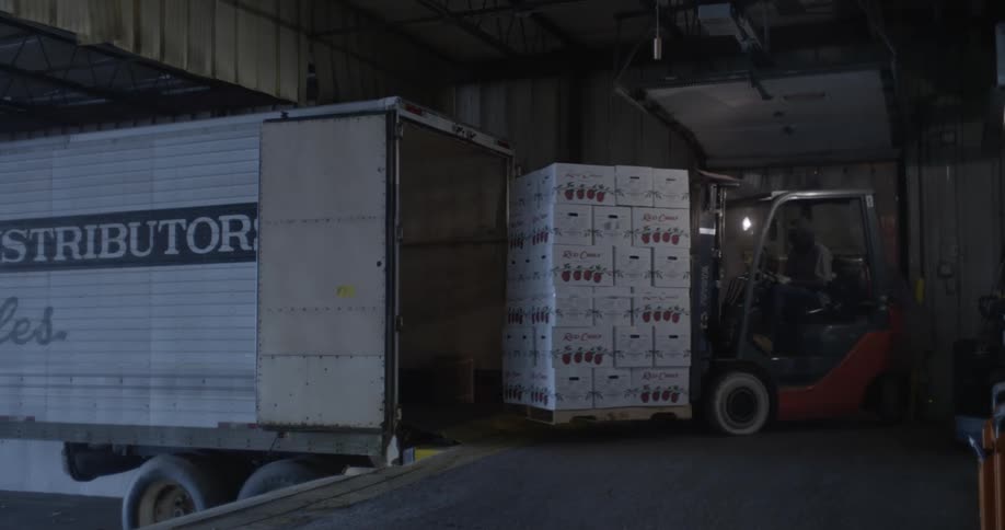 Forklift operator carries a pallet full of products out of the warehouse into a truck