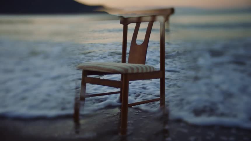 A chair is sitting on a beach as waves roll into shore and under its legs on the sand