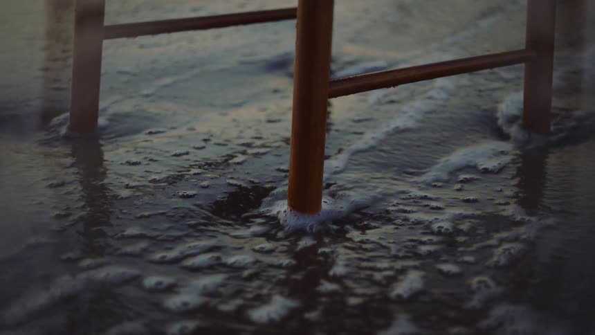 Wooden chair legs in the sand while a wave crashes against it
