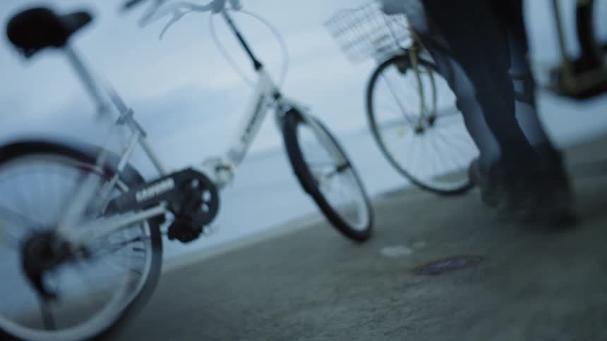 A man is walking a bicycle at the beach and someone is standing near another bike with him