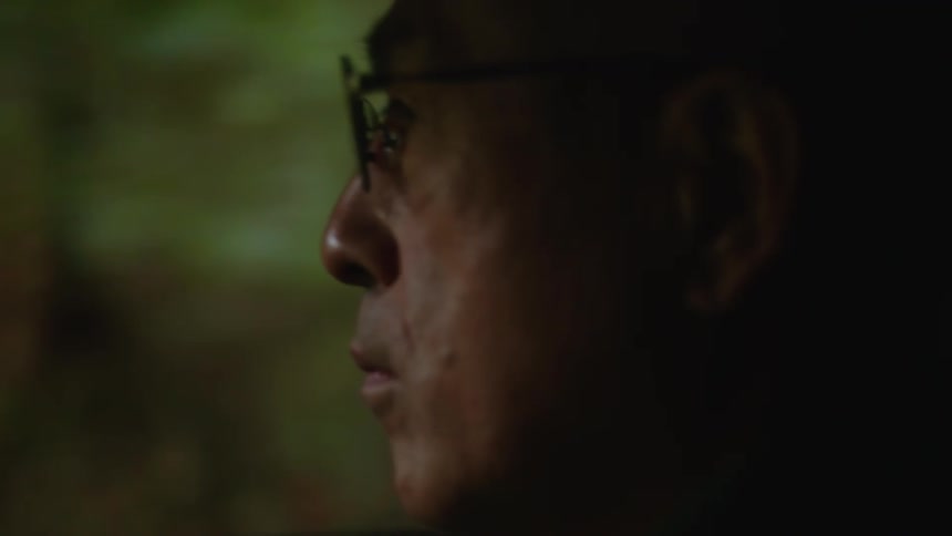 An older man wearing glasses looks ahead while traveling in a vehicle
