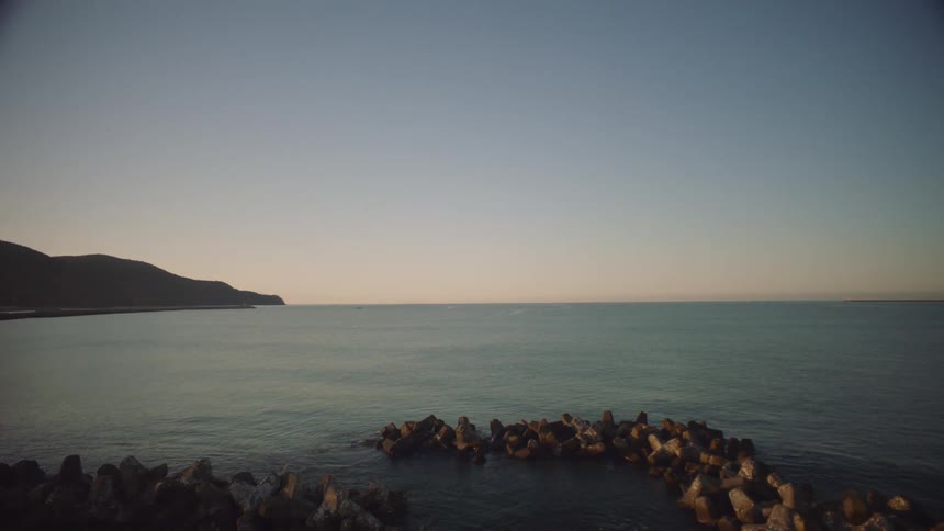 Waves roll into shore as they splash against rocks in the water along the coast under a clear sky