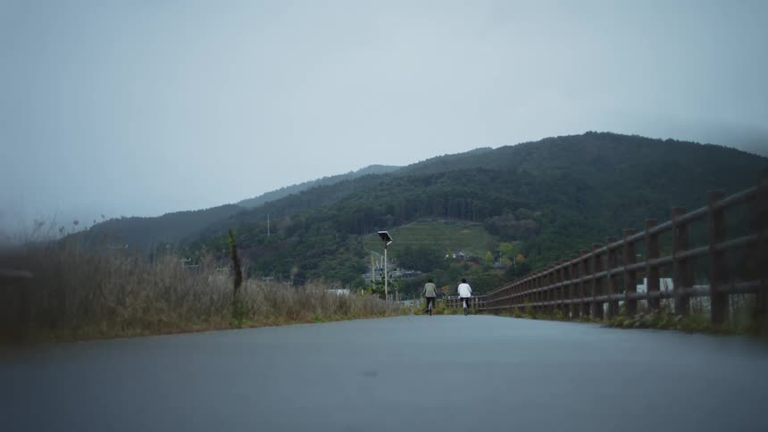 Two people cycle along a path in front of a large hill