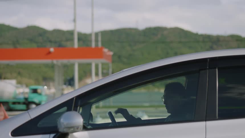 An older man is walking into his car that is parked at a gas station