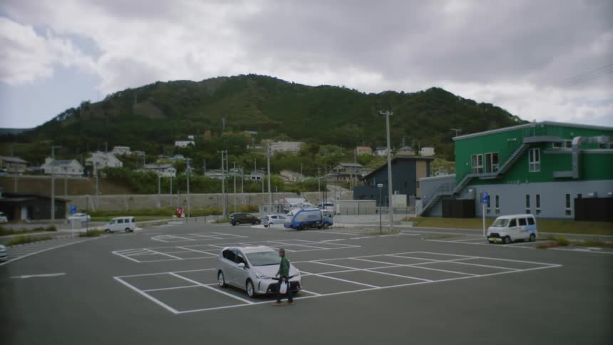 Man carrying a plastic bag walks to his car in the parking lot at daytime