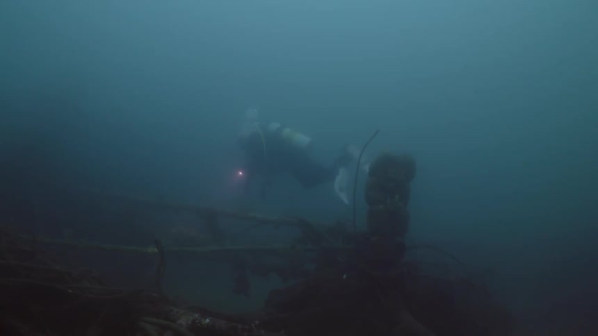 Scuba diver with light swims through murky water examining shipwreck