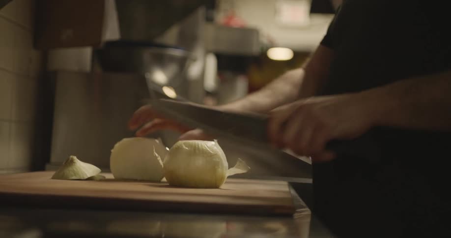 A man is cutting onions in a restaurant kitchen