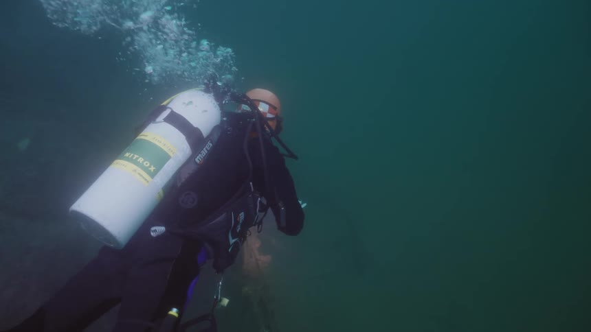 A scuba diver swimming in murky water with a flashlight