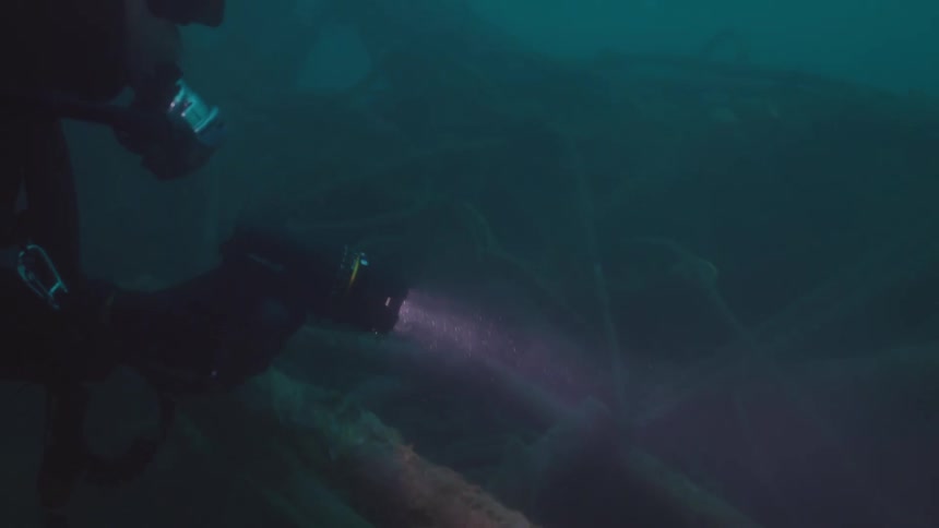 Scuba diver shines a light over the corroded remains of a shipwreck