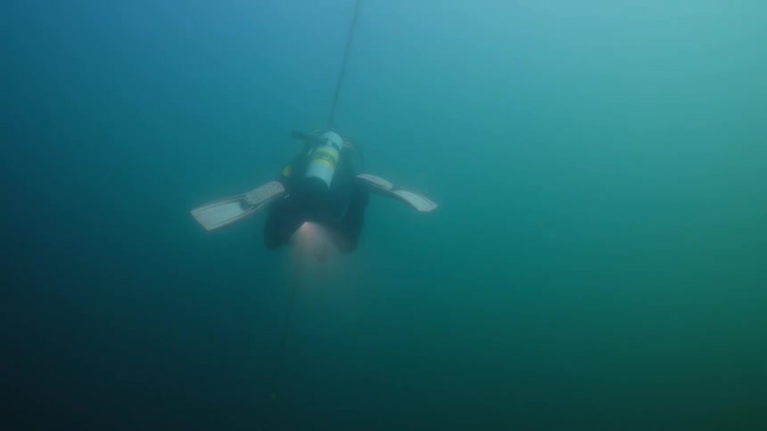 A scuba diver is carrying a flashlight and air bubbles rise as they swim