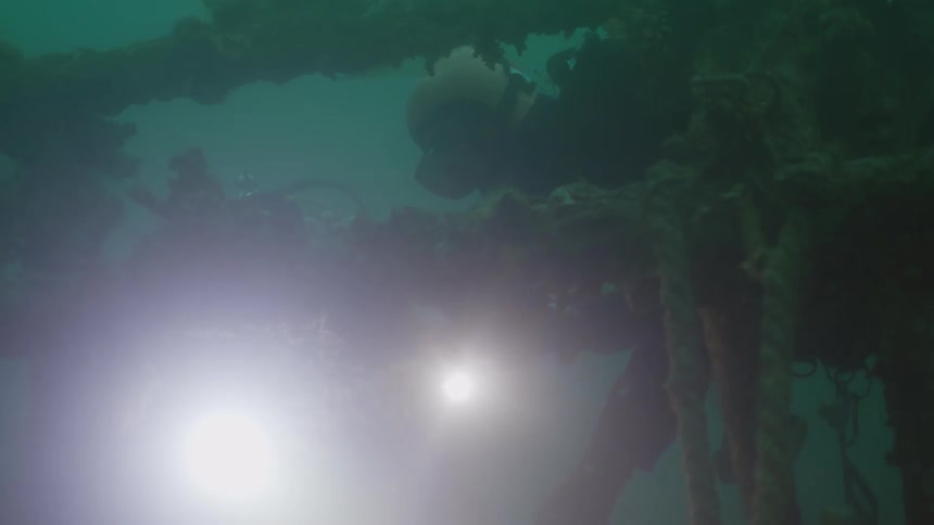 Scuba divers swim underwater near shipwreck