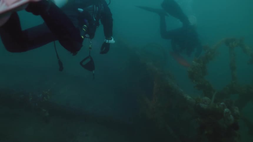 A pair of divers examine wreckage on the sea floor using flashlights