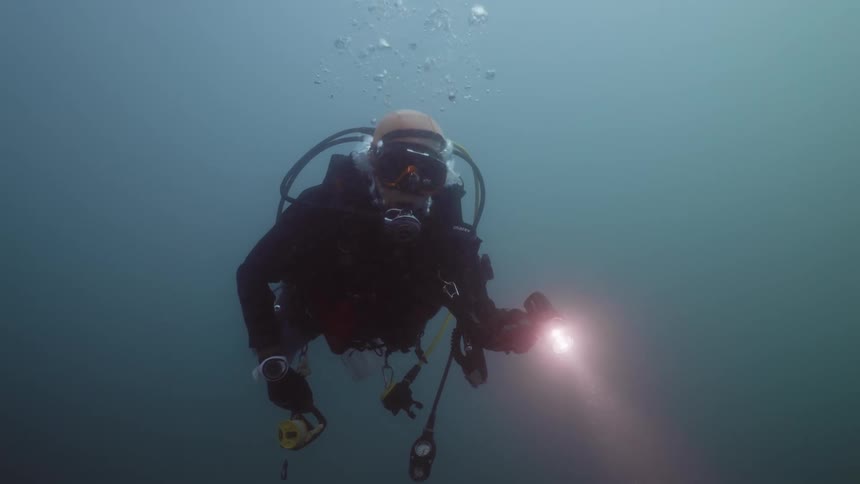 A diver underwater holds a flashlight a treads water