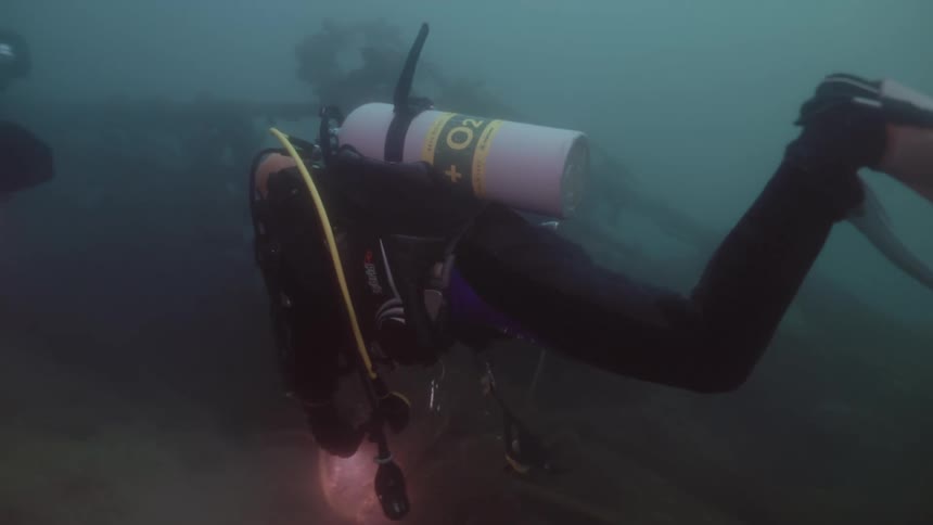 A pair of divers examine wreckage on the sea floor with flashlights
