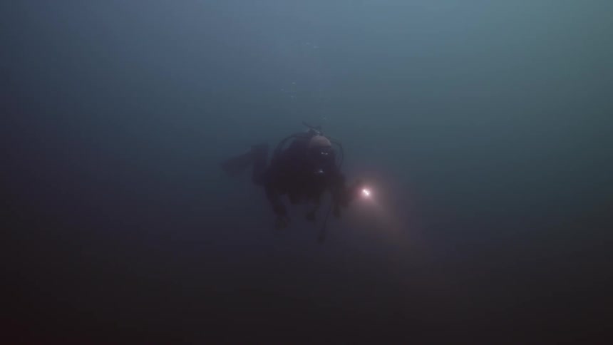 A diver uses a flashlight while swimming underwater