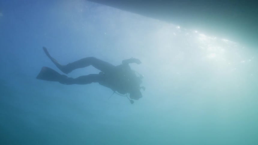 Scuba diver wearing flippers and wetsuit swims underwater