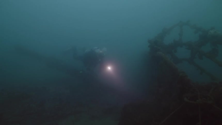 Scuba diver swims through murky water investigating shipwreck