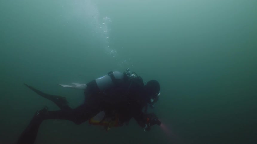 Two divers shine flashlights as they swim under water