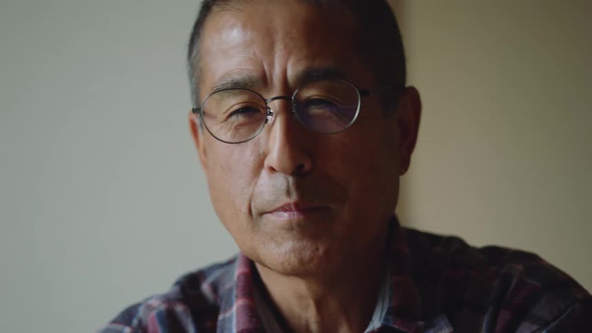 An older man is sitting down inside of his bedroom