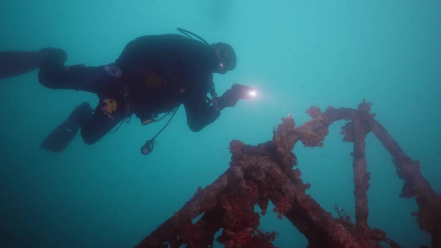 Scuba diver shines a light over the corroded remains of a shipwreck