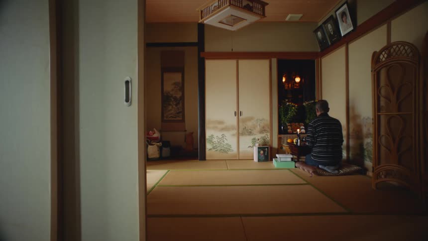 An older man is sitting down on the floor of his bedroom