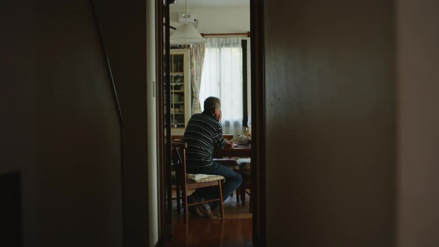 A man sits at a dining room table while lost in thought during the day