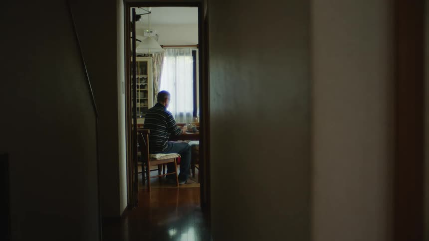 An older man is sitting down on a chair inside of his home