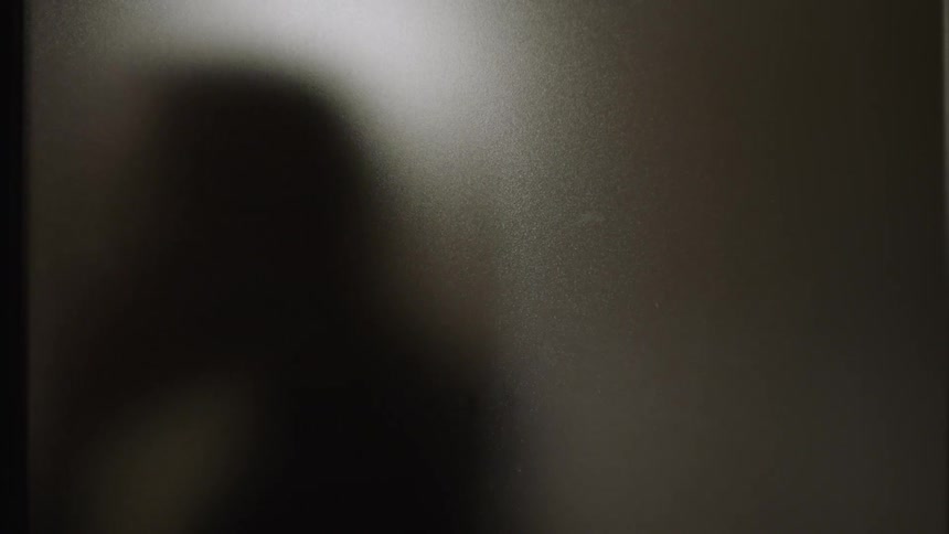 Silhouette of a man talking on a phone passing by a textured glass window