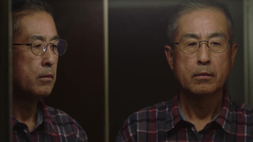 A man looks at his reflection in a mirror with a stern expression