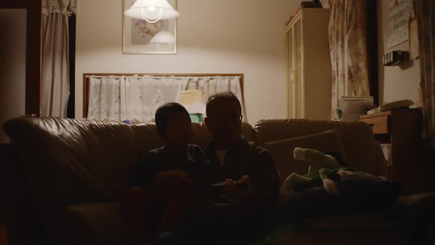 Father and son are sitting down on the couch inside of there home