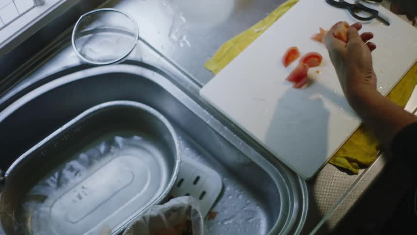 A man cuts a tomato on a cutting board next to the sink